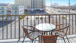 Ein Balkon mit Korbstühlen und einem Glastisch, mit Blick auf einen Parkplatz und ein Hotelgebäude.
