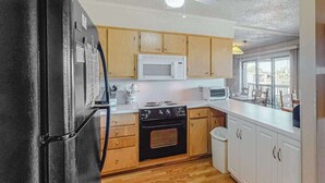 A kitchen with wooden cabinets, a black refrigerator, a white microwave, and a stove. - Our Place At The Beach 306F (Ocean City)
