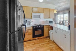 Une cuisine avec des meubles de rangement en bois, un réfrigérateur noir, un four à micro-ondes blanc et une cuisinière.
