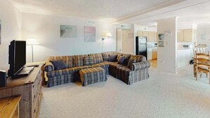 A living room with a sectional sofa, a television, and a lamp. - Our Place At The Beach 306F (Ocean City)