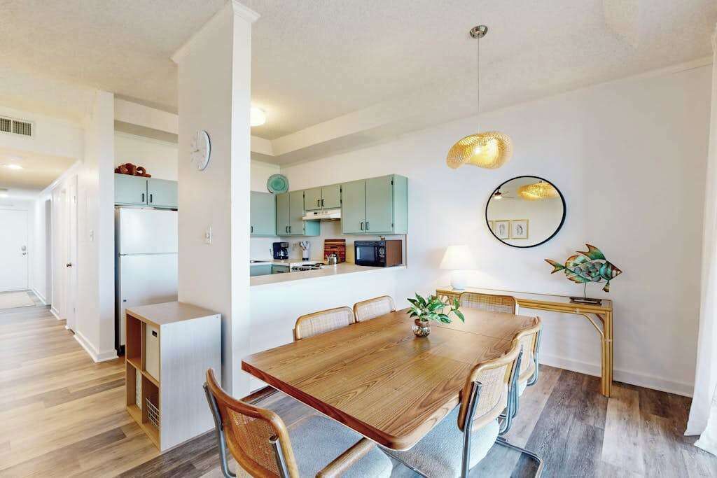 A modern kitchen with a dining area, white walls, and a wooden dining table.