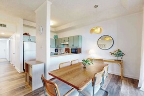 A modern kitchen with a dining area, white walls, and a wooden dining table. - Our Place At The Beach 304C (Ocean City)