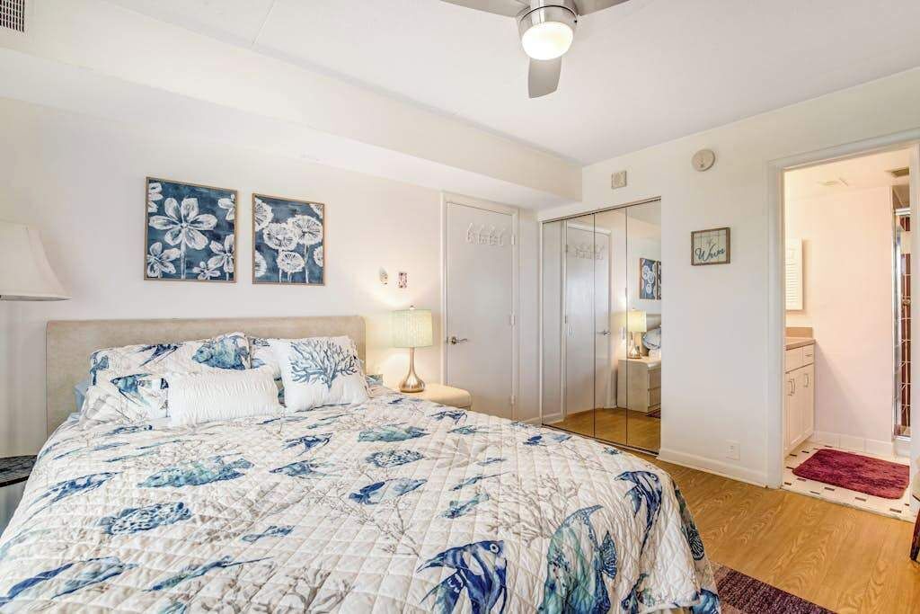 Et soveværelse med en seng, et natbord, en lampe og en dør til et badeværelse.