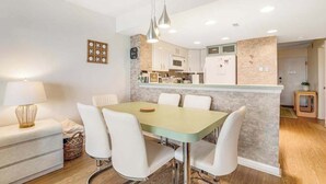Een eethoek met een tafel en stoelen, een keuken op de achtergrond en een lamp op een bijzettafeltje.