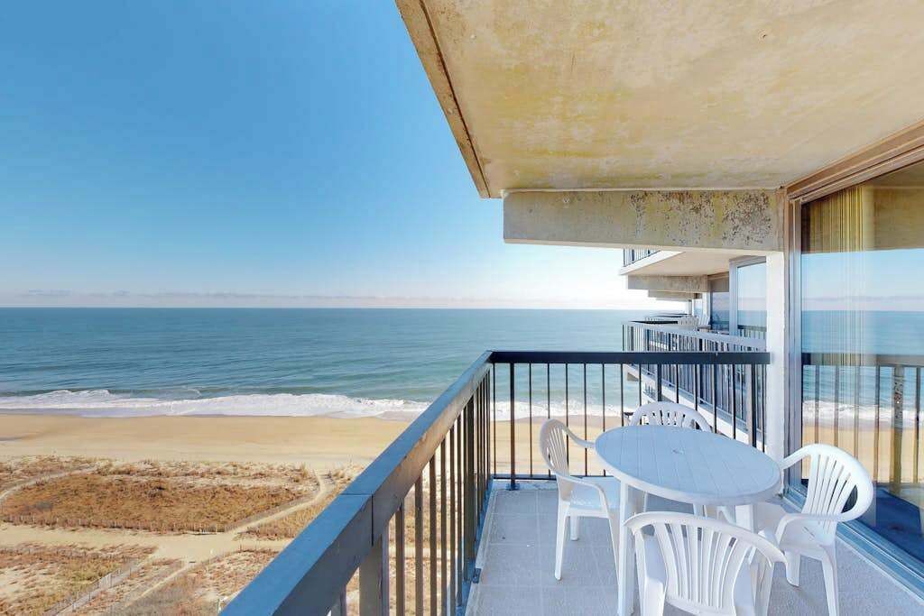 A balcony with a view of the ocean, white plastic chairs, and a small table.