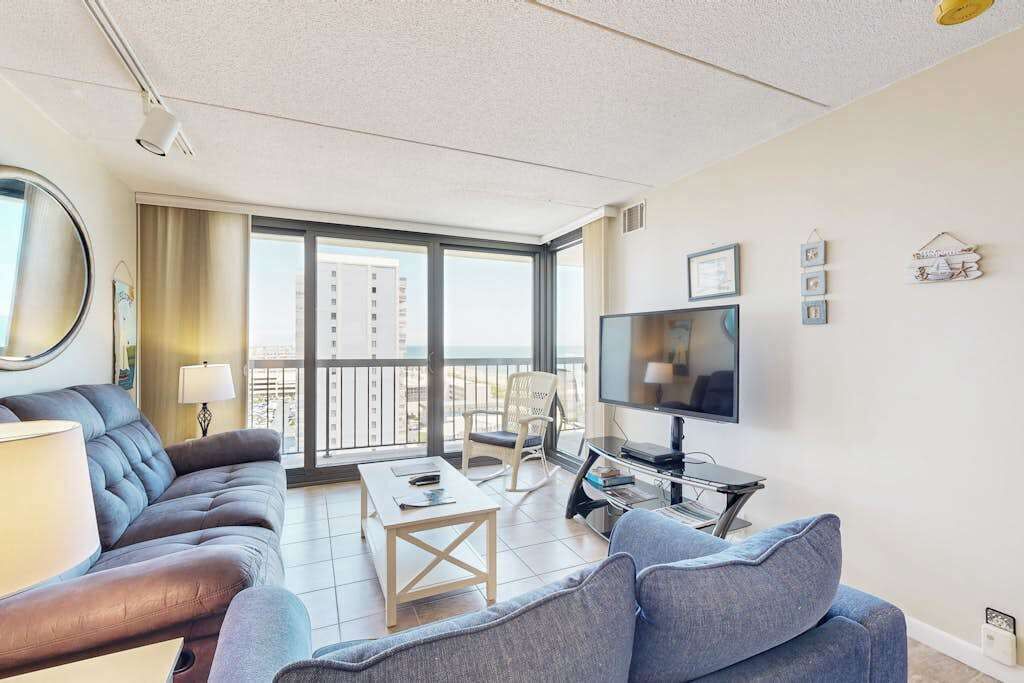 A modern living room with a sofa, coffee table, TV, and a balcony with a view.