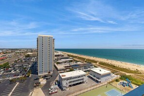 A high-rise building with a parking lot and a beach in the background. - Beach condo with balcony, W/D, pools, game room, tennis & gym (Ocean City)