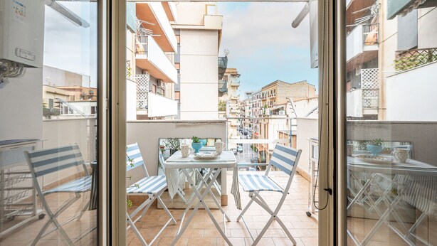 A balcony with a table and chairs, a view of buildings, and a door with a handle. - D Ossuna Central Home by Wonderful Italy (Palermo)