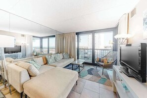 Ein modernes Wohnzimmer mit Sofa, Fernseher und einem Balkon mit Vorhängen.