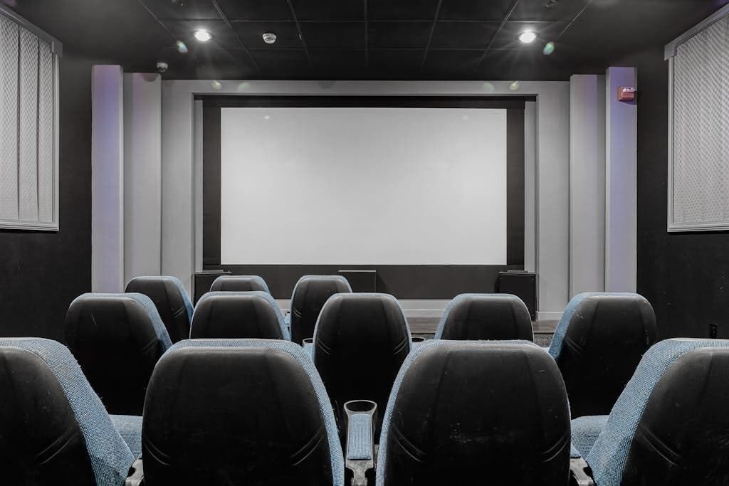A conference room with a large screen, rows of chairs, and a podium.