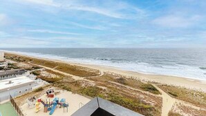 A beach view with a playground, a building, and a path leading to the beach. - Ocean-view getaway with balcony, AC, pools, saunas, tennis & gym (Ocean City)