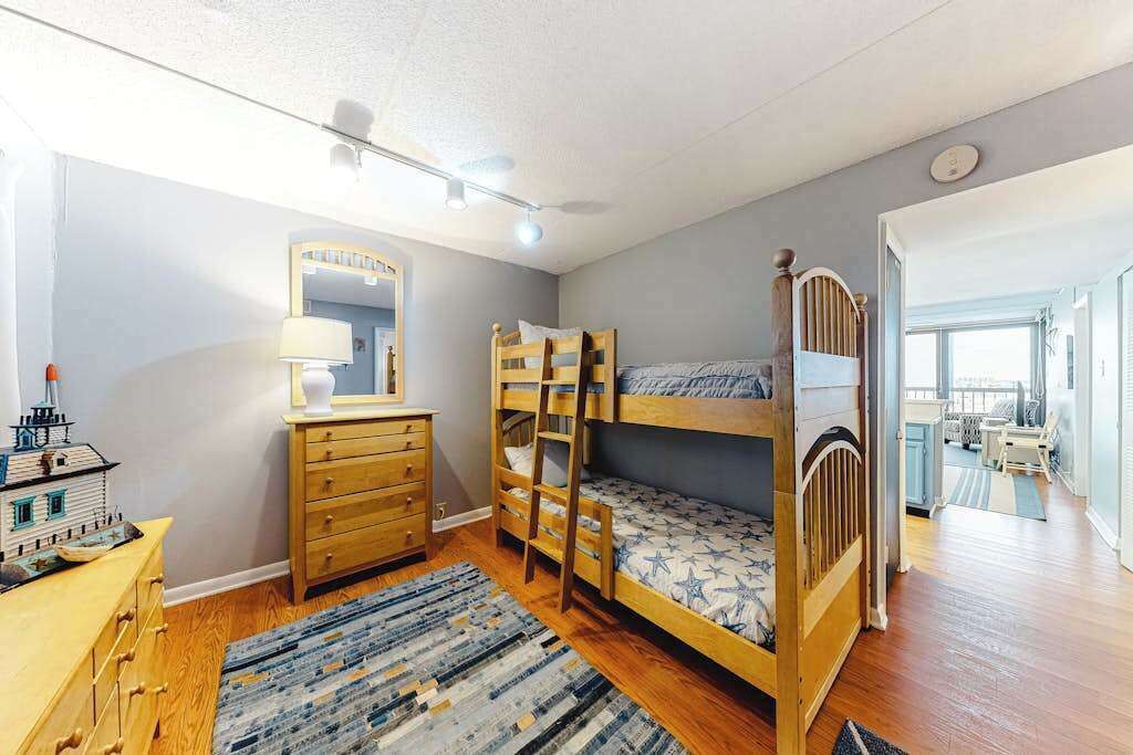 A room with bunk beds, a dresser, a mirror, and a window.
