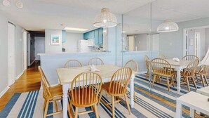 A modern kitchen with a central island, wooden chairs, and a striped rug. - Ocean-view getaway with balcony, AC, pools, saunas, tennis & gym (Ocean City)