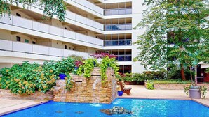 A hotel with a swimming pool, a stone waterfall, and a multi-story building with balconies. - Ocean-view getaway with balcony, AC, pools, saunas, tennis & gym (Ocean City)