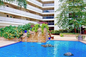 Ein Hotel mit Swimmingpool, einem Stein-Wasserfall und einem mehrstöckigen Gebäude mit Balkonen.