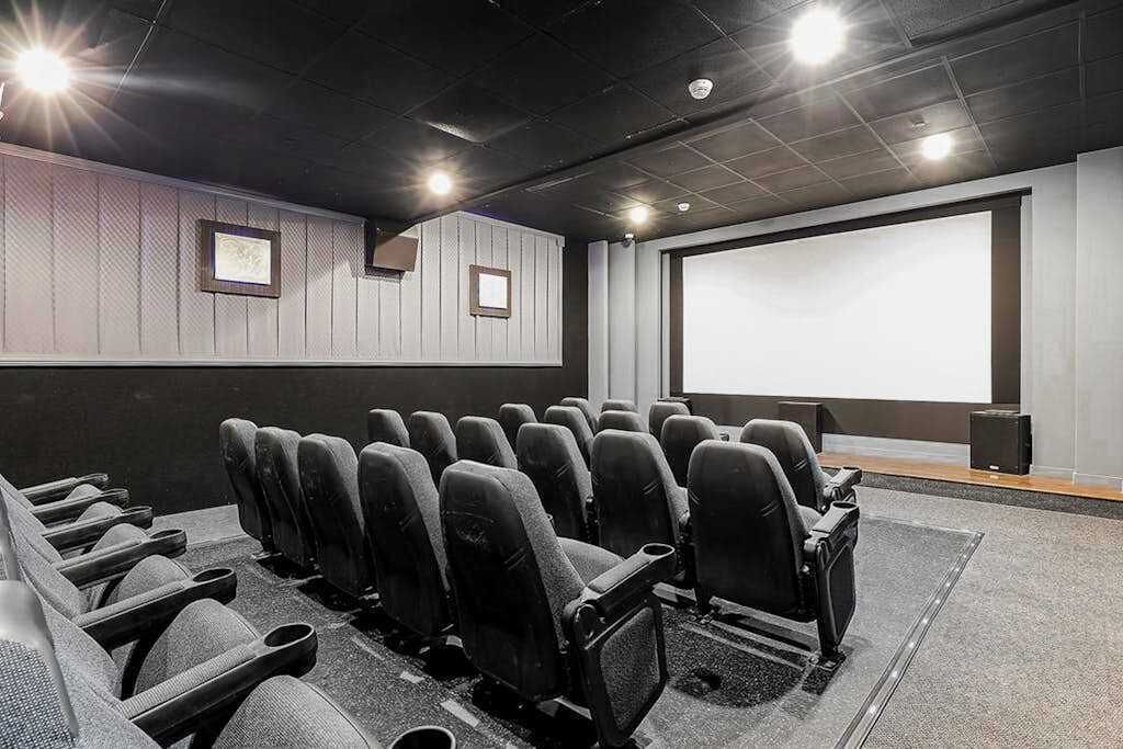 Ein Theater mit Reihen schwarzer Sitze, einer großen Leinwand und einem Lautsprecher auf der rechten Seite.