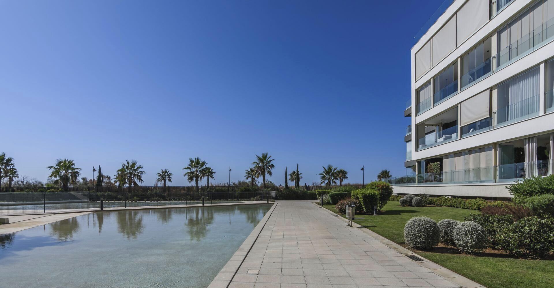 A modern building with a pool, palm trees, and a clear blue sky.