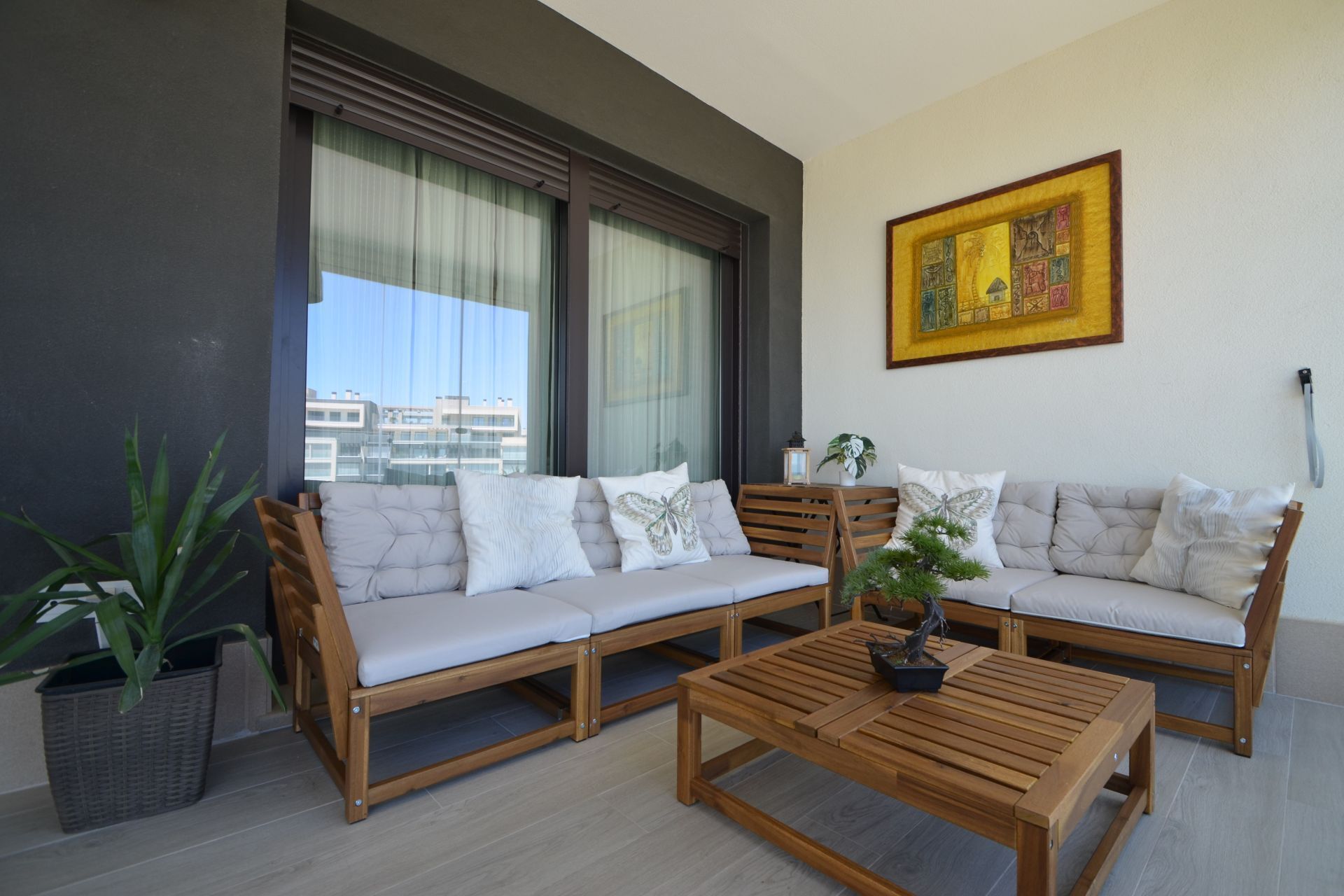 Een balkon met een loungeset, een houten tafel en een bloempot.