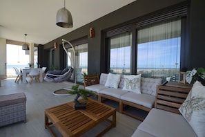Ein modernes Wohnzimmer mit einer Couch, einem Hängesessel, einem Couchtisch aus Holz und Blick auf den Strand.