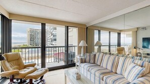 Amplia sala de estar con un ventanal, un sofá, un sillón y un televisor.