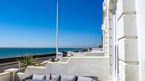 Une terrasse sur le toit avec des sièges extérieurs, une vue sur la mer et un bâtiment aux murs blancs.
