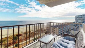 A balcony with a view of the beach and ocean, a wicker sofa, and a small table. - Updated, oceanfront condo with furnished balcony, fast WiFi, central AC & pool (Ocean City)