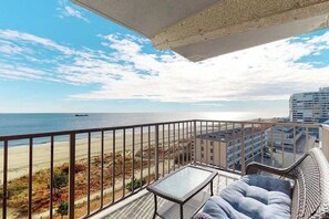 Ein Balkon mit Blick auf Strand und Meer, eine Korbsitzgruppe und ein kleiner Tisch.