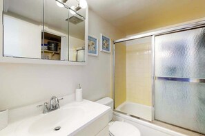 Une salle de bain avec un lavabo blanc, un miroir, des toilettes et une douche à parois de verre.
