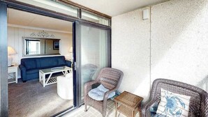 A room with a blue sofa, a wicker chair, a small table, and a glass door leading to another room. - Updated, oceanfront condo with furnished balcony, fast WiFi, central AC & pool (Ocean City)