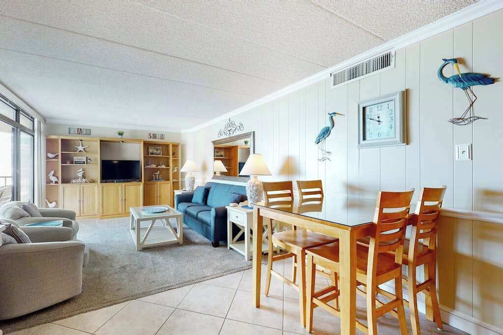 A living room with a TV, sofa, dining table, chairs, and decorative wall art.