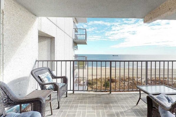 A balcony with wicker furniture, a view of the beach, and a clear sky. - Updated, oceanfront condo with furnished balcony, fast WiFi, central AC & pool (Ocean City)
