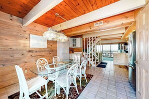 A wooden interior with a dining area featuring a glass table and white chairs, a staircase, and a kitchen area. - Three-Story Oceanfront Townhouse w/Private Deck, Great Views, Central A/C (Ocean City)