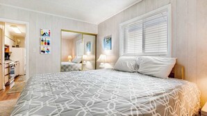 Quarto com cama, abajures, espelho e janela com persianas.