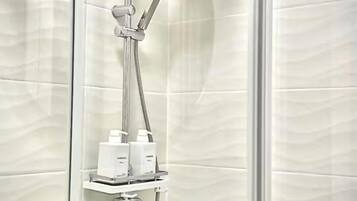 Una doccia con cabina in vetro, dotata di un soffione a mano e uno fisso sul soffitto, un pannello di controllo e uno scaffale con due flaconi.