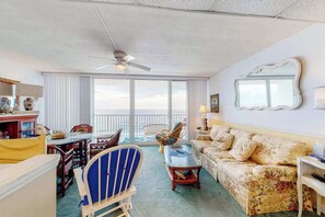 Ein Zimmer mit Deckenventilator, einer Couch, einem Sessel, einem Tisch und einem Balkon mit Blick.