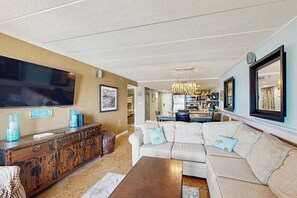 A living room with a sofa, a wooden cabinet, a flat-screen TV, and a chandelier. - Sandpiper Dunes 504 (Ocean City)