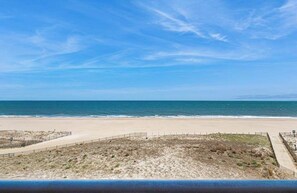 A beach view with a clear sky, sandy shore, and a fenced area. - Sandpiper Dunes 504 (Ocean City)