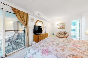 A hotel room with a bed, a television on a wooden dresser, a chair, a glass door leading to a balcony, and a painting on the wall. - Sandpiper Dunes 212 (Ocean City)