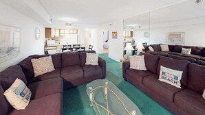 A living room with two dark brown sofas, a coffee table, and a kitchen in the background. - Sandpiper Dunes 212 (Ocean City)