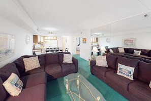 A living room with two dark brown sofas, a coffee table, and a kitchen in the background. - Sandpiper Dunes 212 (Ocean City)