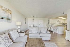 A modern living room with a sofa, a coffee table, and a dining area with chairs. - Sunny condo with balcony, W/D, pools, tennis & AC (Ocean City)