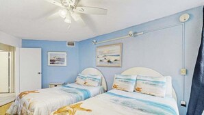 A bedroom with two beds, a ceiling fan, and artwork on the walls. - Oceanfront Condo with a Shaded Balcony, AC, WiFi, Laundry & Shared Pool (Ocean City)