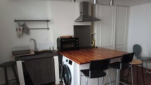Ett kompakt kök med en köksö i mitten, en tvättmaskin, en mikrovågsugn och ett handfat.
