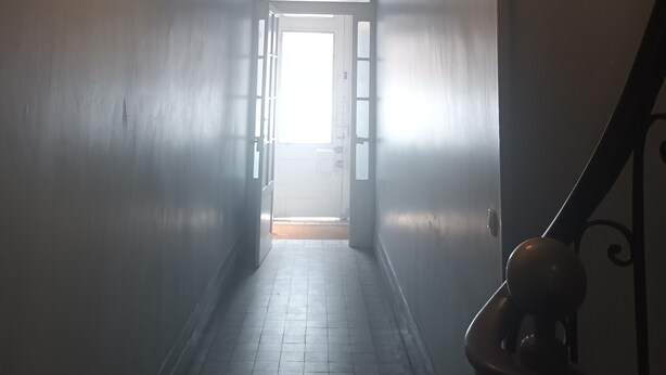 En smal hall med en lampa, en dörr längst ner och en stol på höger sida.