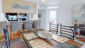 Een kamer met een strandthema, voorzien van een keukenhoek, een eettafel met placemats, en uitzicht op het strand.