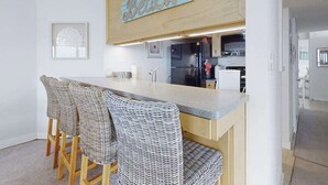 Een keuken met een bar, rieten stoelen en een houten bord waarop 'Beach' staat.
