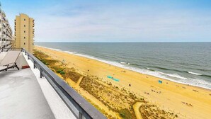 Uitzicht op een strand met een gebouw aan de linkerkant, zandstrand en de oceaan.