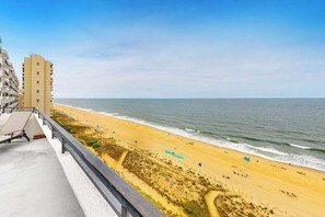 Uitzicht op een strand met een gebouw aan de linkerkant, zandstrand en de oceaan.