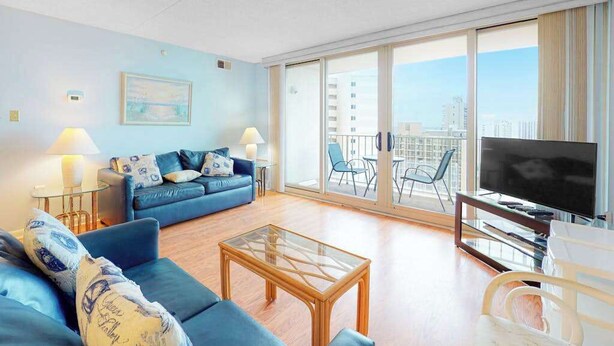 Ein modernes Wohnzimmer mit Sofa, Couchtisch, Fernseher und Balkon mit Sitzgelegenheiten.