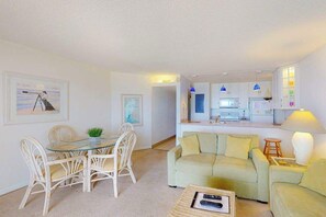 Ein Wohnzimmer mit Esstisch, zwei Sofas, einer Küchenzeile und gerahmten Kunstwerken an den Wänden.